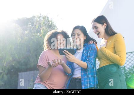 Beim Anschauen von Videos auf dem Smartphone lächeln drei Freundinnen zusammen und genießen gemeinsam Stockfoto