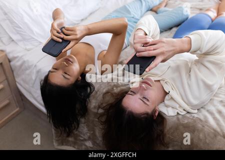Auf dem Bett liegen, zwei Freundinnen mit Smartphones und zu Hause entspannen Stockfoto