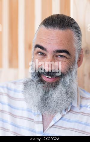 Lächelnder bärtiger Seniorenmann in gestreiftem Hemd posiert für Porträt drinnen Stockfoto