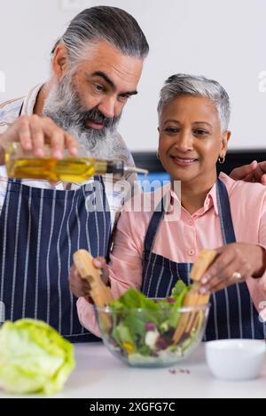 Seniorenpaar bereitet gemeinsam Salat vor, gießt Olivenöl und mischt Zutaten Stockfoto