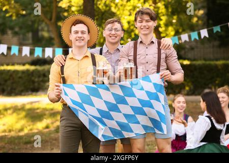 Junge Männer in traditioneller Kleidung mit bayerischer Flagge feiern das Oktoberfest im Freien Stockfoto