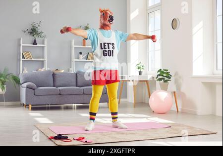 Lustiger junger Mann in Kopfpferdemaske, der Sport-Fit-Übungen mit Hanteln zu Hause macht. Stockfoto