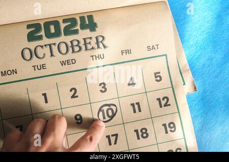 Hand zeigt auf das Datum vom 10. Oktober 2024 auf der flachen Kalenderfläche mit blauem Hintergrund. Welttag der psychischen Gesundheit, Kuba Unabhängigkeit und Curacao Tag. Stockfoto