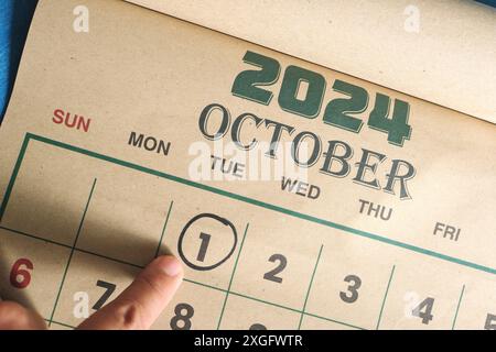 Hand zeigt auf das Datum vom 1. Oktober 2024 auf der flachen Kalenderfläche mit blauem Hintergrund. Erinnerung am ersten Tag des Monats. Stockfoto