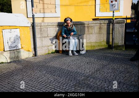 Ein Künstler, der auf einem kleinen Hocker sitzt, kreiert ein Gemälde in einer sonnendurchfluteten Ecke der Dom-Luís-I-Brücke Stockfoto