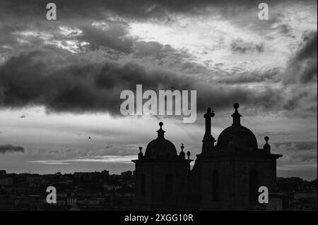 Einfarbige Silhouetten von Vögeln, die in der Abenddämmerung über die Kuppeldächer von Porto fliegen, schaffen eine dramatische Szene vor einem bewölkten Himmel Stockfoto