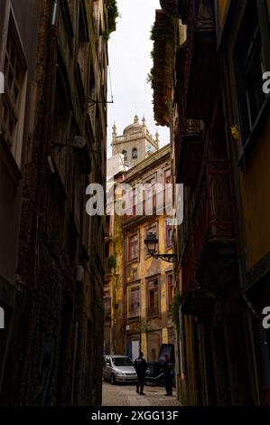 Die enge, schattige Gasse in Porto zeigt die komplizierten Details historischer Gebäude, die zu einem Paar Polizisten und einem Kirchturm führen Stockfoto