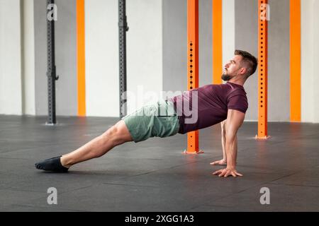 Seitenansicht eines fokussierten Mannes, der im modernen Fitnesscenter Calisthenics-Reverse Plank-Übungen auf dem Boden durchführt Stockfoto