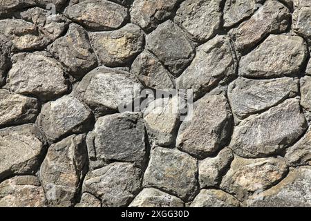 Granitwand, Hintergrund. Oberfläche der aus Granitgesteinen (Ziegeln) gebauten Steinstruktur. Die Wandtextur vulkanischer grauer Farbe. Grauer Zaun Stockfoto