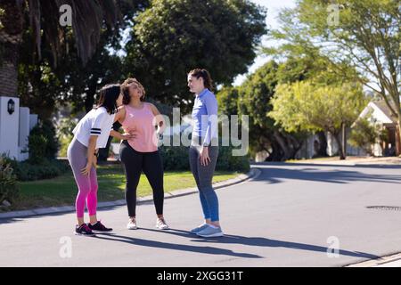 Im Freien trainieren, drei Freundinnen machen Pause und plaudern auf der Straße Stockfoto