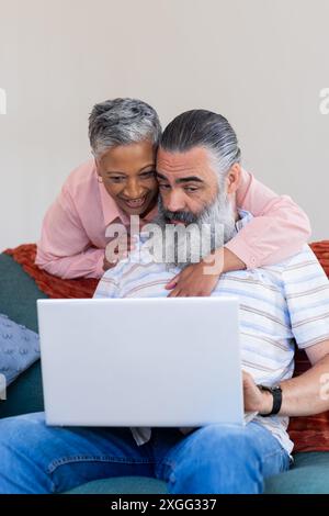 Seniorenpaar, das zusammen ein Notebook benutzt, lächelt und die Zeit zu Hause genießt Stockfoto