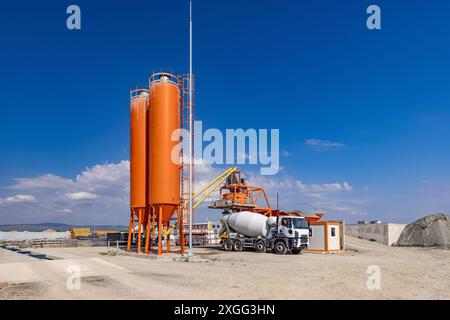 Betonmischanlage mit Mischturm und Zementwagen, die unter klarem Himmel geparkt sind Stockfoto