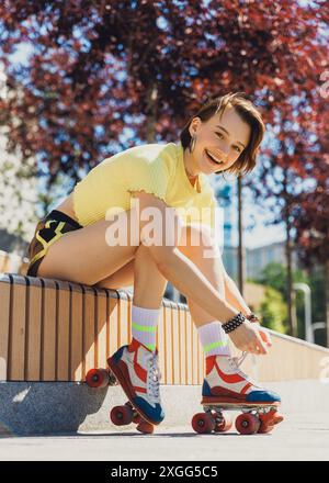 Sportliches, fröhliches junges Mädchen, Teenager schnürt sich Schnürsenkel auf Retro-Rollschuhläufern und macht sich bereit für das Training an sonnigen Tag im Park. Stockfoto