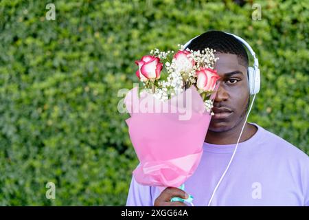 Afrikanischer Mann, der ein Gesicht mit einem Rosenstrauß in einem lila Hemd versteckt, hält Blumen. Stockfoto