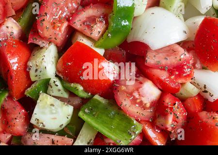 Die Nahaufnahme eines frischen Gemüsesalats mit Tomaten, grüner Paprika und Zwiebeln, gewürzt mit Kräutern und Olivenöl, zeigt die Texturen des Frischs Stockfoto