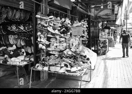 Ein Mann läuft an einem Schuhgeschäft vorbei mit einem Schild mit der Aufschrift "2 für 1 Dollar". Der Laden ist voll mit vielen verschiedenen Arten von Schuhen, einschließlich Sneakers, Loafers, A Stockfoto