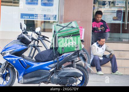 Ein Mann sitzt auf einer Stufe neben einem Motorrad mit einem grünen Kasten drauf. Auf der Schachtel steht das Wort „GREIF“ Stockfoto