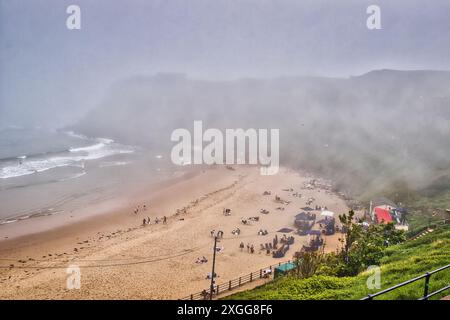 Eine neblige Strandszene mit Menschen, die sich auf dem Sand entspannen, und ein paar Zelten, die mit Wellen aufgerichtet sind, die sanft auf die Küste stürzen, Großbritannien, Europa Stockfoto