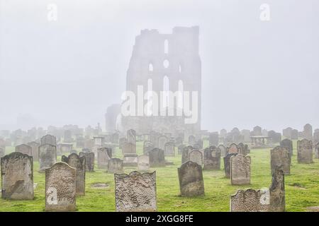 Ein nebeliger Friedhof mit alten Grabsteinen und einem großen, alten, ruinierten Gebäude im Hintergrund, Großbritannien, Europa Stockfoto