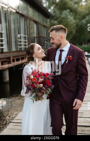 Das erste Treffen der Braut und des Bräutigams in Hochzeitskleidern am Pier in der Nähe des Wassers Stockfoto