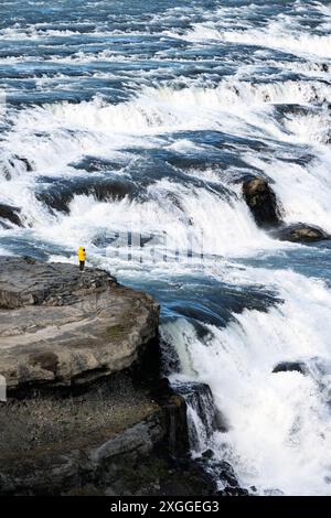 Atemberaubende Aussicht auf den Gullfoss Wasserfall mit einem Touristen in einer gelben Jacke. Gullfoss ist der beliebteste Wasserfall in Island und einer der beliebtesten Wasserfälle Stockfoto