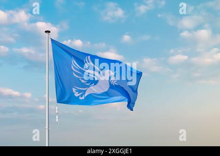 Wehende blaue Friedensfahne mit weißer Taube, die einen Olivenzweig vor einem stimmungsvollen blauen Himmel hält Stockfoto