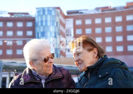 Zwei ältere Frauen lächeln sich vor einem Krankenhaus an. Die Szene ist warm und vertraut Stockfoto