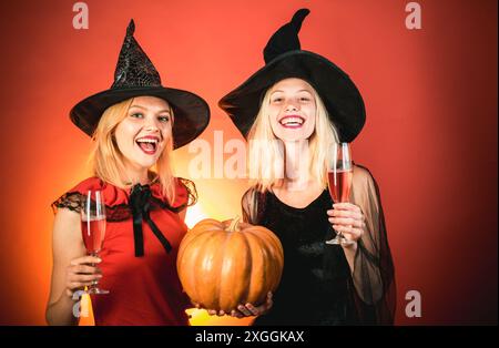 Zwei schöne blonde Frauen in Karnevalskostümen. Zwei emotionale junge Frauen in halloween-Kostümen auf Party über orangem Hintergrund mit Kürbis. Festlich Stockfoto