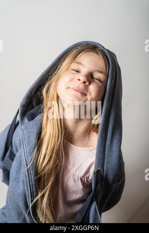 Das junge Mädchen tanzt gerne in einer grauen Jacke. Ihr langes, blondes Haar schwebt durch die Luft. Ihr Gesicht strahlt eine fröhliche Lebensfreude aus Stockfoto