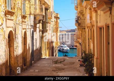 Enge Gasse der Altstadt von Senglea von Malta. Alte europäische Straße mit Blick auf das Boot, das im Wasser angedockt ist Stockfoto