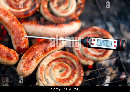 Nahaufnahme gegrillter Würstchen auf dem Grill mit digitalem Thermometer, das die Temperatur in der Celsius-Vorlage anzeigt Stockfoto