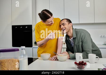 Ein junges schwules Paar frühstückt gemeinsam in einem modernen Apartment, wobei ein Partner den anderen spielerisch mit Müsli versorgt. Stockfoto