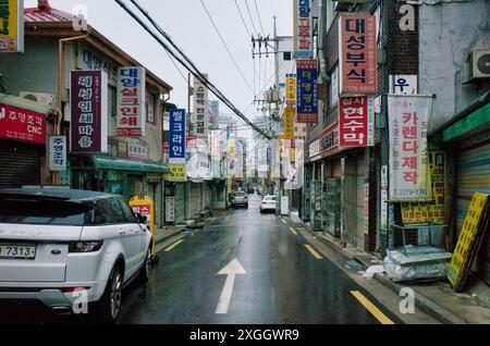 Enge, regnerische Straße in Seoul, gesäumt von bunten Schildern und Geschäften, die das geschäftige Stadtleben einfangen Stockfoto