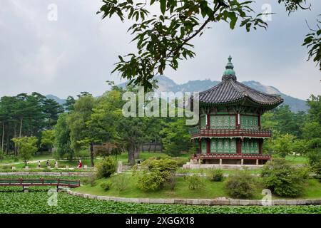 Ruhiger koreanischer Palastpavillon mit Blick auf den Lotusteich, umgeben von üppigen Gärten und fernen Bergen. Stockfoto