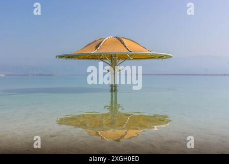 Der große Sonnenschirm spiegelt sich im blauen Wasser der Küste des Toten Meeres in der Ferienstadt ein Bokek, Israel. Stockfoto