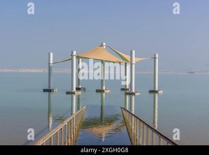 Der große Sonnenschirm spiegelt sich im blauen Wasser der Küste des Toten Meeres in der Ferienstadt ein Bokek, Israel. Stockfoto