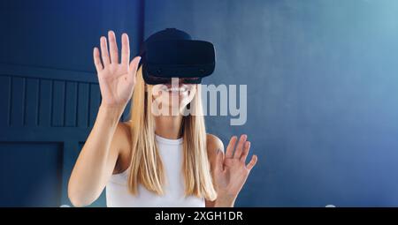 Eine junge Frau mit blondem Haar trägt ein VR-Headset und lächelt, während sie mit der virtuellen Umgebung interagiert. Stockfoto