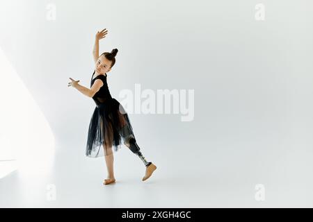 Ein junges Mädchen in schwarzem Trikot und Tutu spielt eine anmutige Pose und zeigt ihr Talent und ihre Entschlossenheit als Turnerin mit einer Beinprothese. Stockfoto