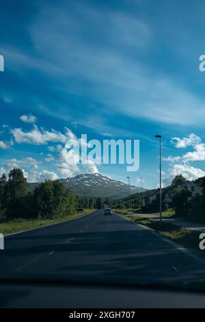 Auf einer Straße auf dem Land, mit einem Berg, der unter blauem Himmel vor sich heraufsteigt, ein Auto davor. Nordnorwegen. Stockfoto