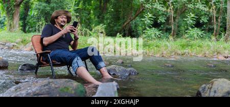 Ein hübscher junger Mann mit Bart in schwarzem Hemd und Jeans reist und spaziert durch die Berge. Im schönen Herbstwald und nutzen Sie seine Intelligenz Stockfoto