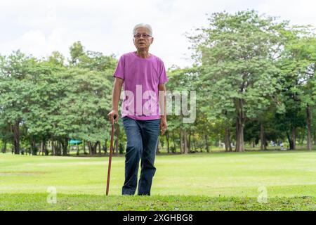 Profilaufnahme eines älteren Mannes, der mit einem Stock in einem Park läuft. Älterer alter Mann mit Gehstock, der in einem öffentlichen Park steht. Senior-Konzept. Stockfoto