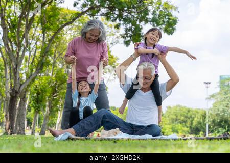 Die Großeltern ließen ihre Enkelin im Park sitzen. Menschen verschiedener Generationen lachen fröhlich im Park auf den Matten. Lustige Meere Stockfoto