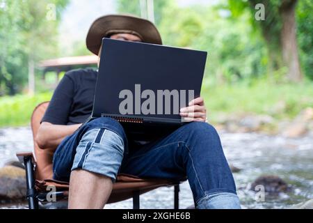 Ein freiberuflicher Mann arbeitet in der Natur im Herbstwald. Landleben. Eine Pause von der Zivilisation. Van Life Vibes. Ein Mann mit Laptop. Abstand l Stockfoto