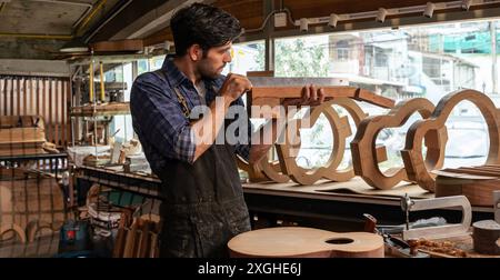 Ein Geigenbauer überprüft einen hohlen Gitarrenhals in seiner Werkstatt, um die Ausrichtung, die Kunst und das Handwerkskonzept zu überprüfen. Ich arbeite an der Entwicklung der Gitarre, wo Stockfoto