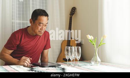 Offen von einem alten asiatischen Rentner, der einen Tablet-Computer benutzt, Text liest, lächelt oder lacht glücklich und positiv. Senior asian mit digitalem Technologiekonzept Stockfoto