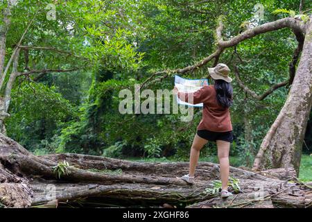 Glückliche Frau beim Wandern und beim Anschauen der Karte im Freien in der Natur. Reisende erkunden die Bergkarte des Waldes. Frau mit Hut und rotem kariertem Hemd, die ein M hält Stockfoto