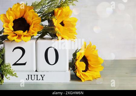 Internationaler Schachtag. Weiße Holzkalenderblöcke mit dem Datum des 20. Juli und wunderschönem Sonnenblumenstrauß mit Bokeh. Selektiver Fokus. Stockfoto