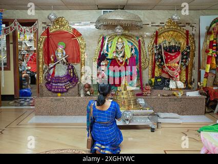 Eine nicht identifizierte Hindufrau betet in einem Tempel. Die Götter von links sind Sarswati, Durga und Kali. Im Wilton Hundu Tempel in Connecticut, 2024. Stockfoto