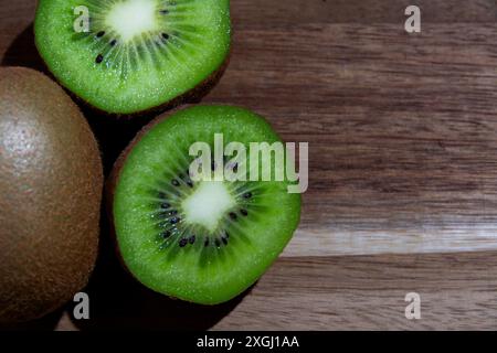 Eine Nahaufnahme einer Kiwi-Frucht wurde in zwei Hälften geschnitten und zeigt ihr lebendiges grünes Fleisch und winzige schwarze Samen, die ordentlich auf einer Holzoberfläche angeordnet sind. Stockfoto