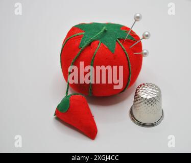 Rotes, Tomatenförmiges Kissen mit grünem Stiel und Blatt, Erdbeerkissen und Metalltaschel auf weißer Oberfläche Stockfoto